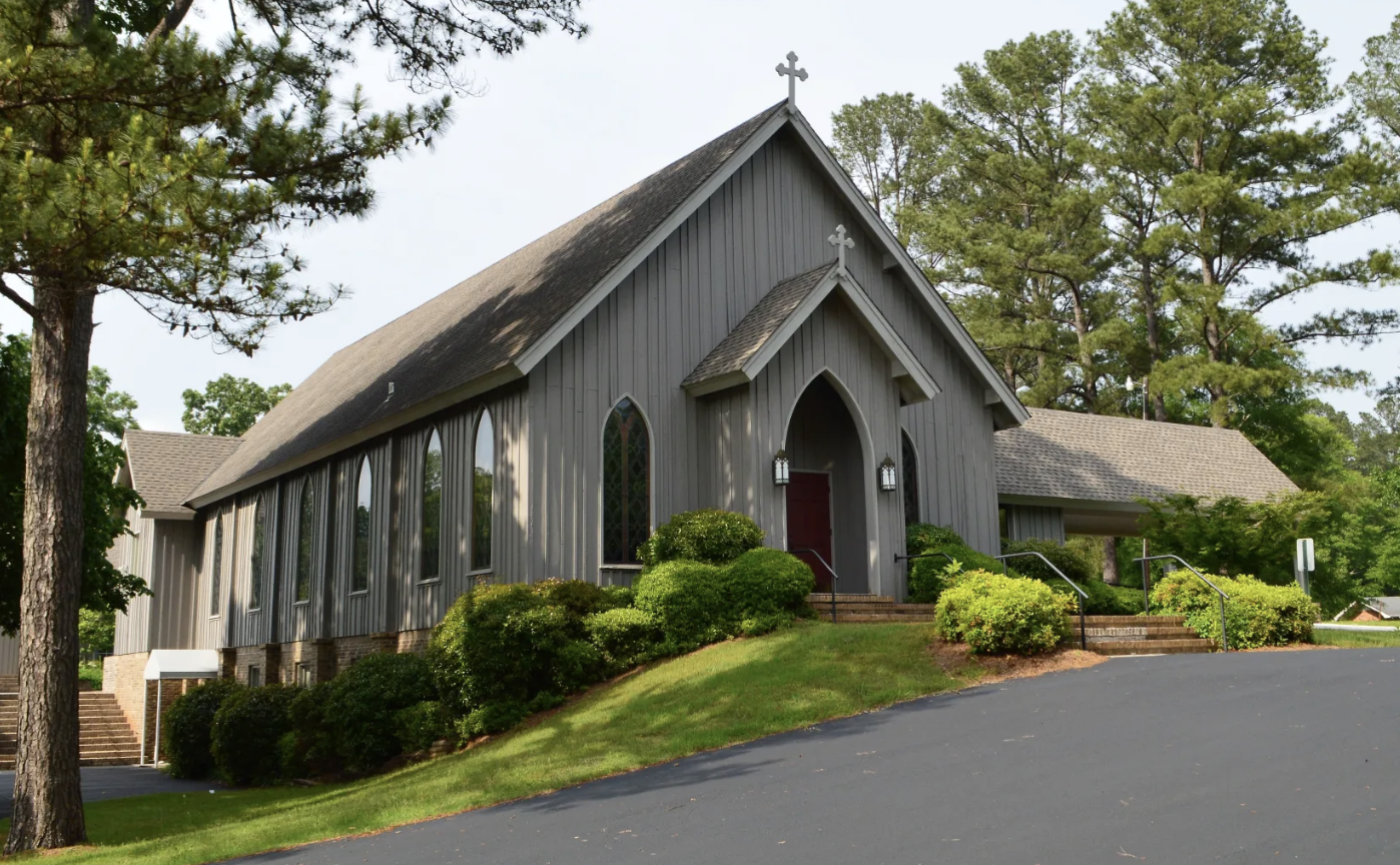 Board-and-batten church with a red door beneath tall pines