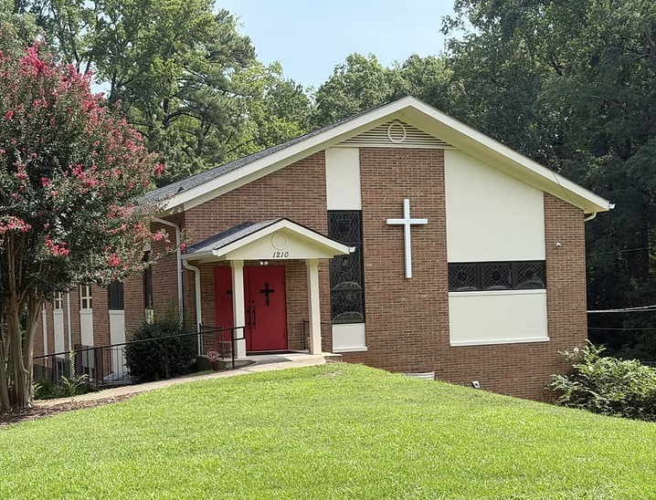 Brick church with red doors beneath summer trees