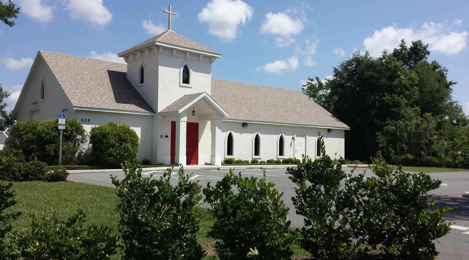 White stucco church with red front doors and a small bell tower